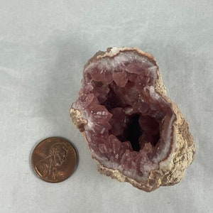 May include: A pink amethyst geode with a natural brown exterior. The geode is open, revealing a cavity lined with sparkling pink crystals.