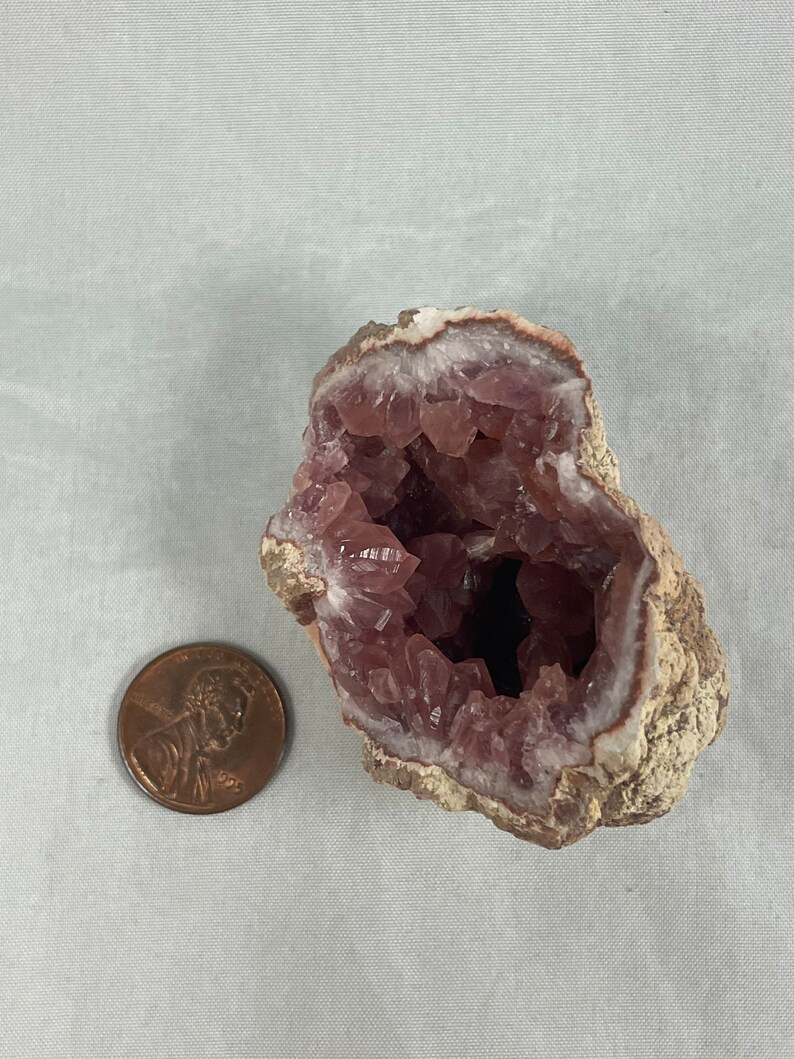 May include: A pink amethyst geode with a natural brown exterior. The geode is open, revealing a cavity lined with sparkling pink crystals.