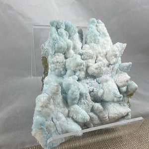 May include: A cluster of blue and white celestite crystals in a clear acrylic display stand. The crystals have a bubbly, textured surface.
