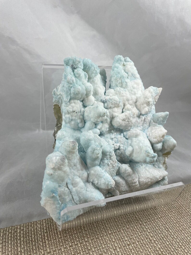 May include: A cluster of blue and white celestite crystals in a clear acrylic display stand. The crystals have a bubbly, textured surface.