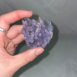 K&ouml;nnte beinhalten: Eine violette Achat-Geode mit einem Cluster aus kleinen, runden, violetten Achat-Kn&ouml;tchen. Die Geode ist eine nat&uuml;rliche Formation mit einer rauen, unregelm&auml;&szlig;igen Form.