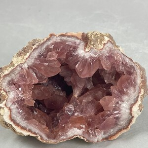 May include: A geode with a pink amethyst crystal interior. The geode is cut in half, revealing the crystals inside. The exterior of the geode is a light brown color.
