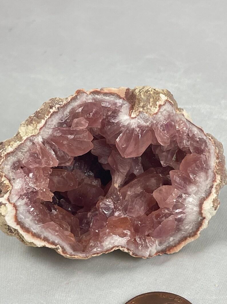 May include: A geode with a pink amethyst crystal interior. The geode is cut in half, revealing the crystals inside. The exterior of the geode is a light brown color.