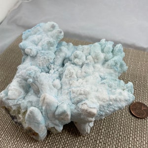 May include: A large, white and blue, naturally formed, crystal cluster. The crystal has a rough, textured surface and appears to be made of many smaller crystals.