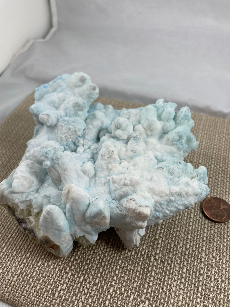 May include: A large, white and blue, naturally formed, crystal cluster. The crystal has a rough, textured surface and appears to be made of many smaller crystals.