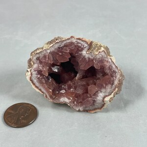 May include: A pink amethyst geode with a hollow center and a rough exterior. The geode is about the size of a US penny.