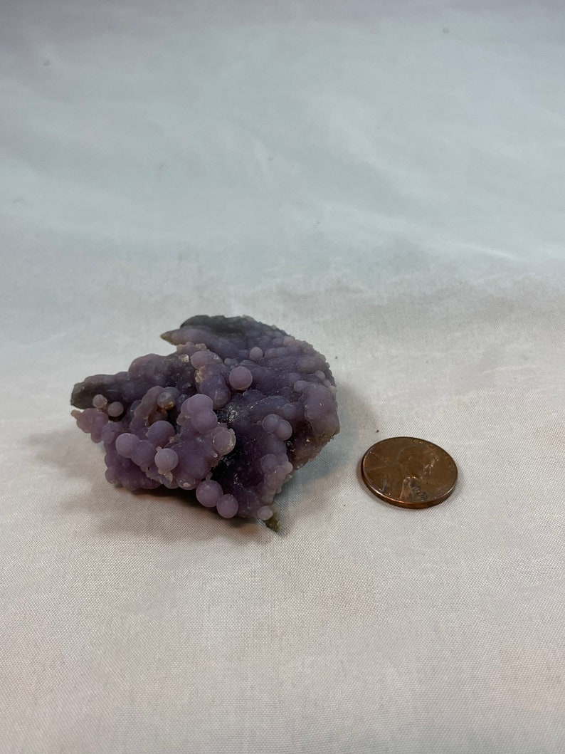 K&ouml;nnte beinhalten: Eine violette Achat-Geode mit einem Cluster kleiner, runder Kn&ouml;tchen. Die Geode ist etwa so gro&szlig; wie ein deutscher Cent.