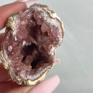 May include: A pink amethyst geode with a natural, rough exterior and a hollow interior lined with sparkling pink crystals.