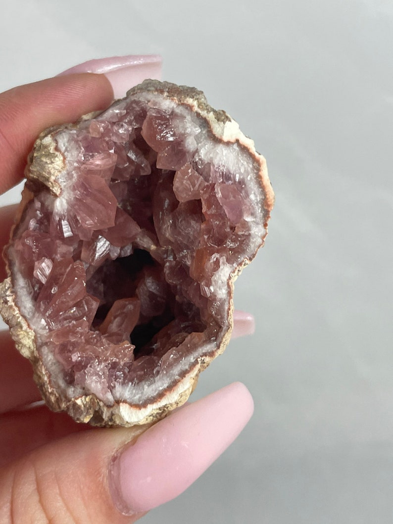 May include: A pink amethyst geode with a natural, rough exterior and a hollow interior lined with sparkling pink crystals.