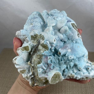 May include: A large, rough, light blue and yellow crystal cluster with a white, powdery coating. The crystal is a natural specimen with a unique, organic shape.