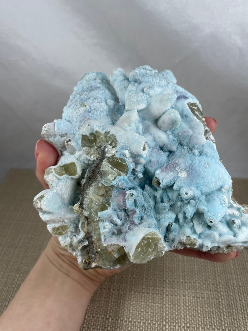 May include: A large, rough, light blue and yellow crystal cluster with a white, powdery coating. The crystal is a natural specimen with a unique, organic shape.