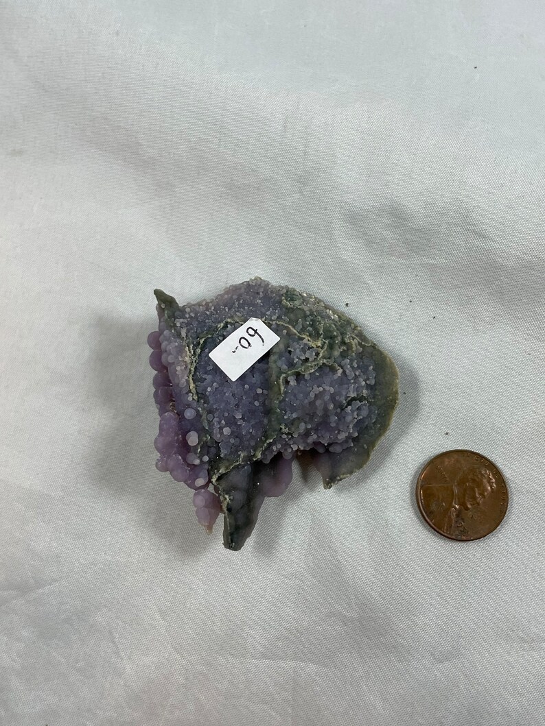 K&ouml;nnte beinhalten: Eine violette und graue Achat-Geode mit einem Etikett, auf dem "99" steht. Die Geode ist etwa so gro&szlig; wie ein deutscher Cent.