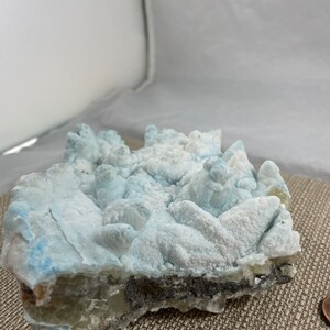 May include: A blue and white crystal cluster with a rough, textured surface. The crystal has a layered structure with a darker, gray layer at the bottom.
