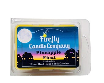 May include: A yellow wax melt in a clear plastic container with a label that reads "Firefly Candle Company Pineapple Float handmade in Hilton Head Island South Carolina". The label has a night sky background with a moon, stars, and a firefly.