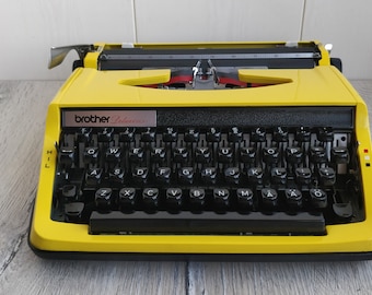 Máquina de escribir Brother Deluxe 800 de los años 70. Portátil. Funciona manualmente. Teclas QWERTY. Color amarillo vintage. Fabricada en Japón.