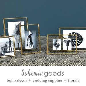 May include: Four gold-toned picture frames with different images inside. The frames are on a black and gold patterned surface. The images include a tropical leaf, a woman in a hat, a flower, and a beach scene.
