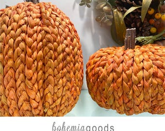 May include: Two woven orange pumpkins with brown stems. The pumpkins are made of a textured material and are in varying sizes. The image also includes the text "bohemiagoods" and "modern rustic + wedding supplies + florals".
