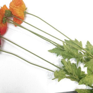 K&ouml;nnte beinhalten: Eine Ansammlung k&uuml;nstlicher Mohnblumen in Rot- und Oranget&ouml;nen, mit gr&uuml;nen Stielen und Bl&auml;ttern, vor einem wei&szlig;en Hintergrund. Das Bild zeigt die leuchtenden Farben und zarten Texturen der Blumen, ideal f&uuml;r die Inneneinrichtung oder Bastelprojekte.