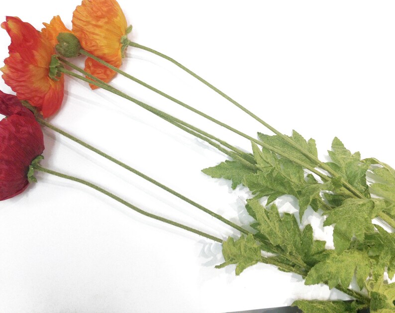 K&ouml;nnte beinhalten: Eine Ansammlung k&uuml;nstlicher Mohnblumen in Rot- und Oranget&ouml;nen, mit gr&uuml;nen Stielen und Bl&auml;ttern, vor einem wei&szlig;en Hintergrund. Das Bild zeigt die leuchtenden Farben und zarten Texturen der Blumen, ideal f&uuml;r die Inneneinrichtung oder Bastelprojekte.