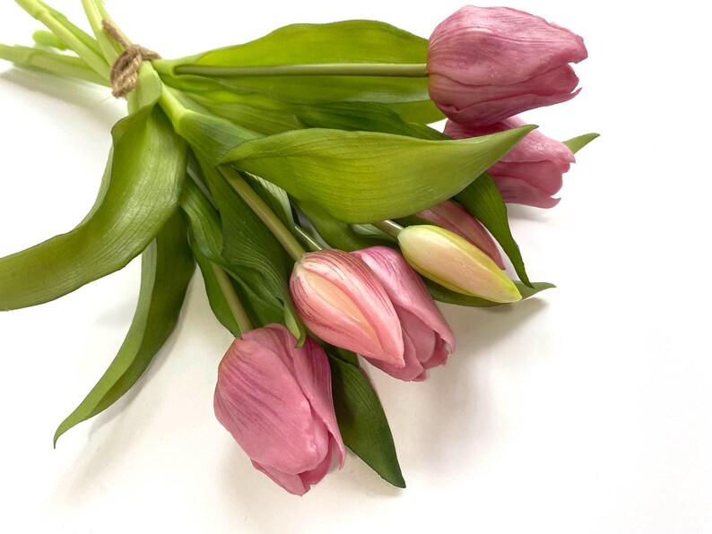 May include: A bouquet of pink tulips with green stems and leaves. The tulips are arranged in a loose, natural way, with some of the flowers overlapping.