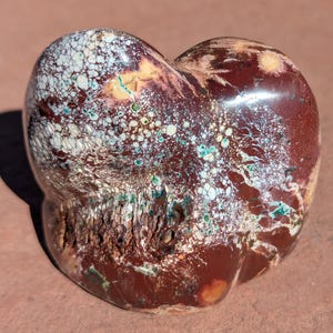 May include: A white ceramic mug with a black handle and the text "But First, Coffee" in a bold, black font. The mug is set against a blurred background, suggesting a cozy setting.