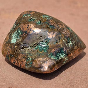 May include: A polished, irregular mineral specimen featuring a metallic bronze and copper-toned surface interspersed with vibrant patches of deep forest green and teal crystalline inclusions, showcasing a smooth, reflective, and textured appearance.