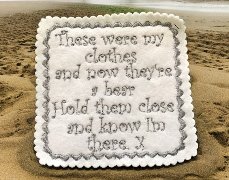 May include: A white felt coaster with a scalloped border and embroidered text in silver thread. The text reads "These were my clothes and now they're a bear. Hold them close and know I'm there. X".