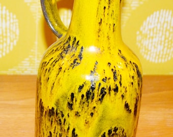May include: A yellow ceramic vase with black glaze, featuring a unique drip effect. The vase has a rounded body and a handle.
