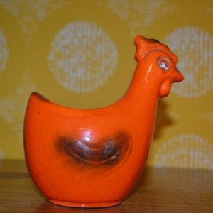 Könnte beinhalten: Orangefarbener Keramik-Hühnertopf mit braunem Glasurdetail. Der Topf ist in Form eines Huhns mit erhobenem Kopf und Schnabel geformt.