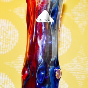 Puede incluir: Un jarrón de vidrio azul y rojo con un diseño ondulado y texturizado. El jarrón tiene una etiqueta que dice "O.Eac."
