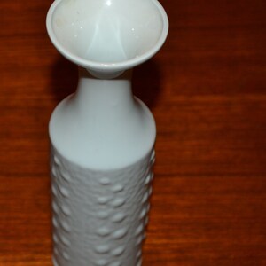 Op de afbeelding: Witte keramische vaas met een getextureerd, bubbelvormig oppervlak. De vaas heeft een brede, uitlopende opening en een smalle hals.