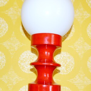 May include: A red ceramic table lamp with a white globe shade. The lamp has a unique, hourglass-shaped base.