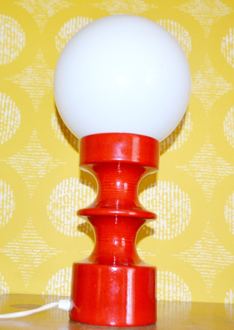 May include: A red ceramic table lamp with a white globe shade. The lamp has a unique, hourglass-shaped base.