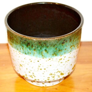 May include: A brown, green, and white ceramic planter with a speckled glaze. The planter has a wide, round opening and a slightly flared base.