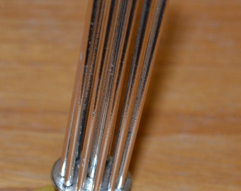 May include: A silver metal stand with a round base and multiple thin metal rods extending upwards. The stand is on a wooden surface.