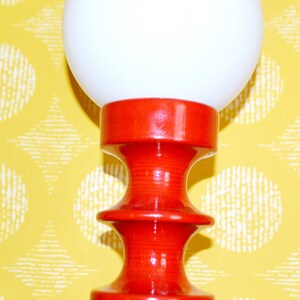 May include: A red ceramic table lamp with a white globe shade. The lamp has a unique, hourglass-shaped base.