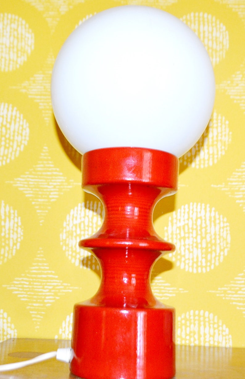 May include: A red ceramic table lamp with a white globe shade. The lamp has a unique, hourglass-shaped base.