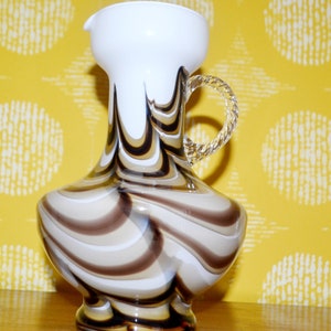 Puede incluir: Una jarra de vidrio blanco y marrón con un patrón de remolino. La jarra tiene un asa blanca y una boca ancha.