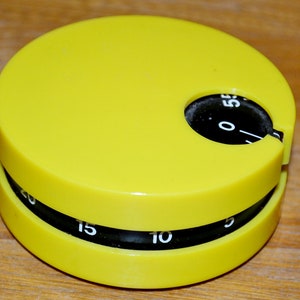 May include: A yellow kitchen timer with black numbers. The timer has a dial that rotates to set the time. The numbers on the dial are 0, 5, 10, 15, and 20.