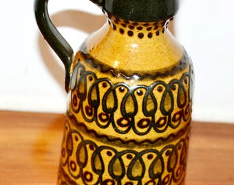 May include: A brown ceramic vase with a black handle and a geometric pattern. The vase has a wide mouth and a narrow base.