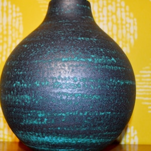 May include: A dark green ceramic vase with a textured surface. The vase has a round body and a narrow neck.