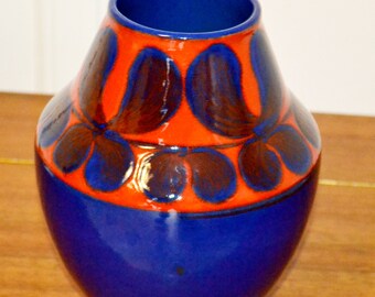 May include: A blue and orange ceramic vase with a geometric pattern. The vase has a rounded body and a narrow opening.