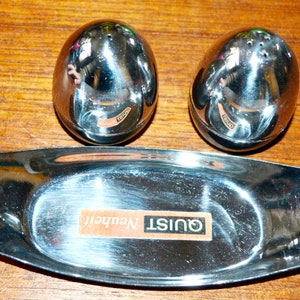 Può includere: Un set di saliera e pepe in argento a forma di uova, con un vassoio in argento abbinato. Il vassoio ha la scritta "Quist Netherlands" stampata su di esso.