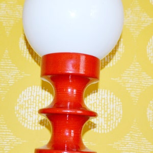 May include: A red ceramic table lamp with a white globe shade. The lamp has a unique, hourglass-shaped base.