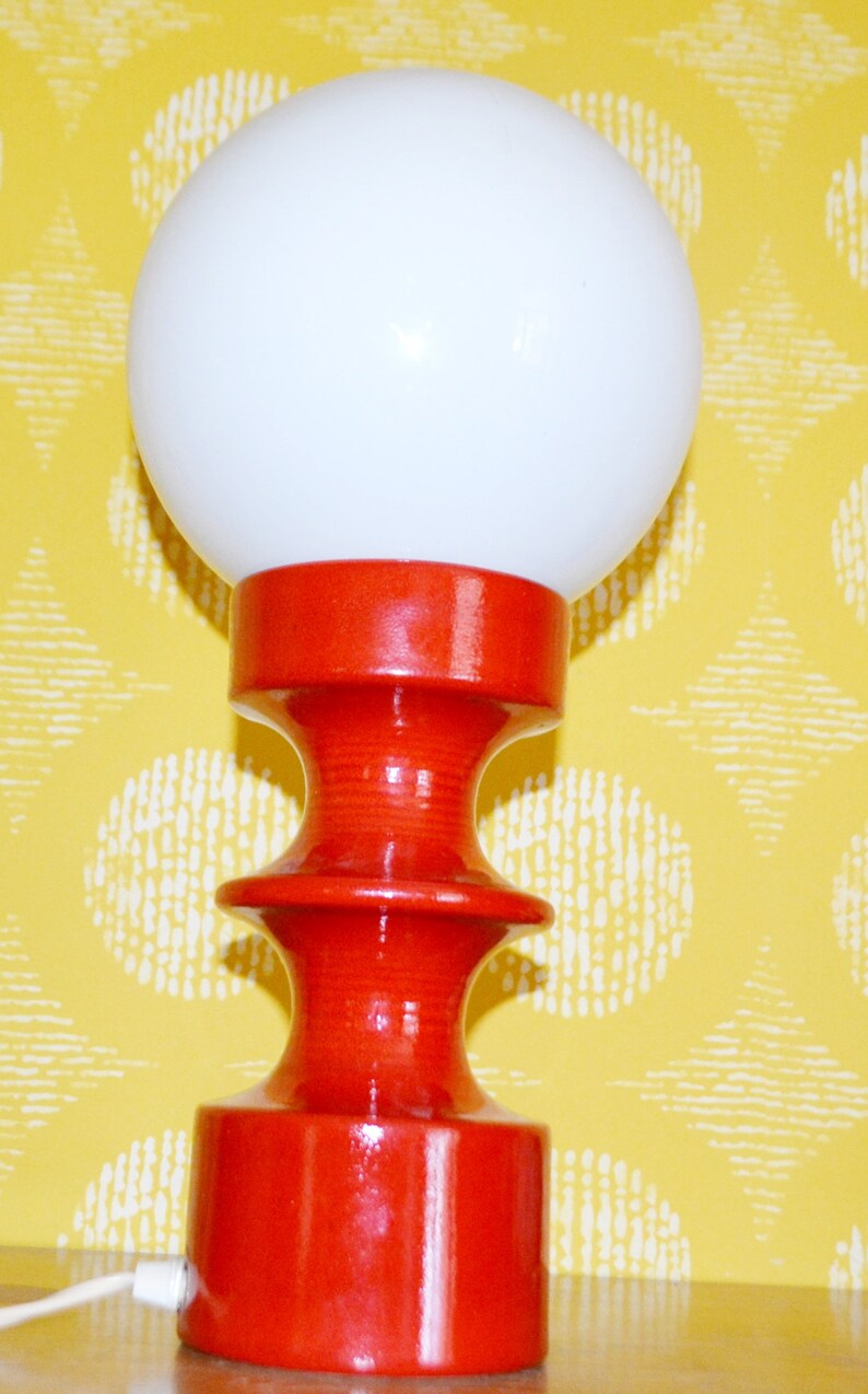 May include: A red ceramic table lamp with a white globe shade. The lamp has a unique, hourglass-shaped base.