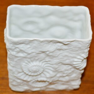 Puede incluir: Jarr&oacute;n de cer&aacute;mica blanca con una superficie texturizada que se asemeja a formaciones rocosas y conchas fosilizadas.