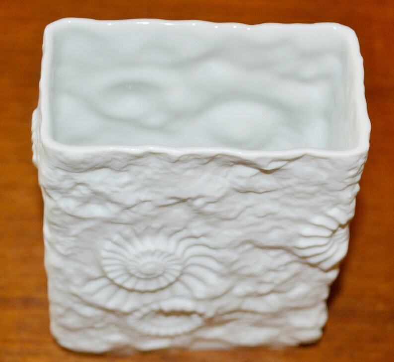 Puede incluir: Jarr&oacute;n de cer&aacute;mica blanca con una superficie texturizada que se asemeja a formaciones rocosas y conchas fosilizadas.