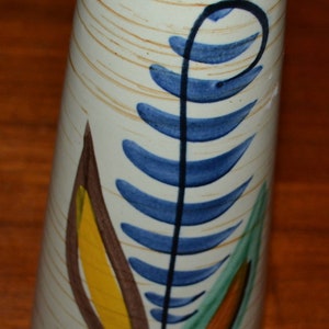 May include: A white ceramic vase with a blue, green, yellow, and brown stylized leaf design.