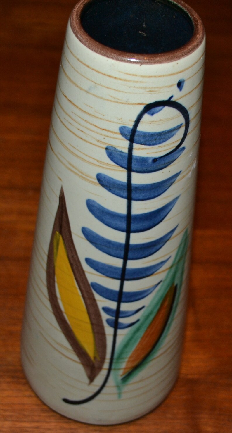 May include: A white ceramic vase with a blue, green, yellow, and brown stylized leaf design.