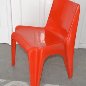 Può includere: Una sedia in plastica arancione brillante con un design moderno e unico. La sedia ha uno schienale alto e una seduta larga.